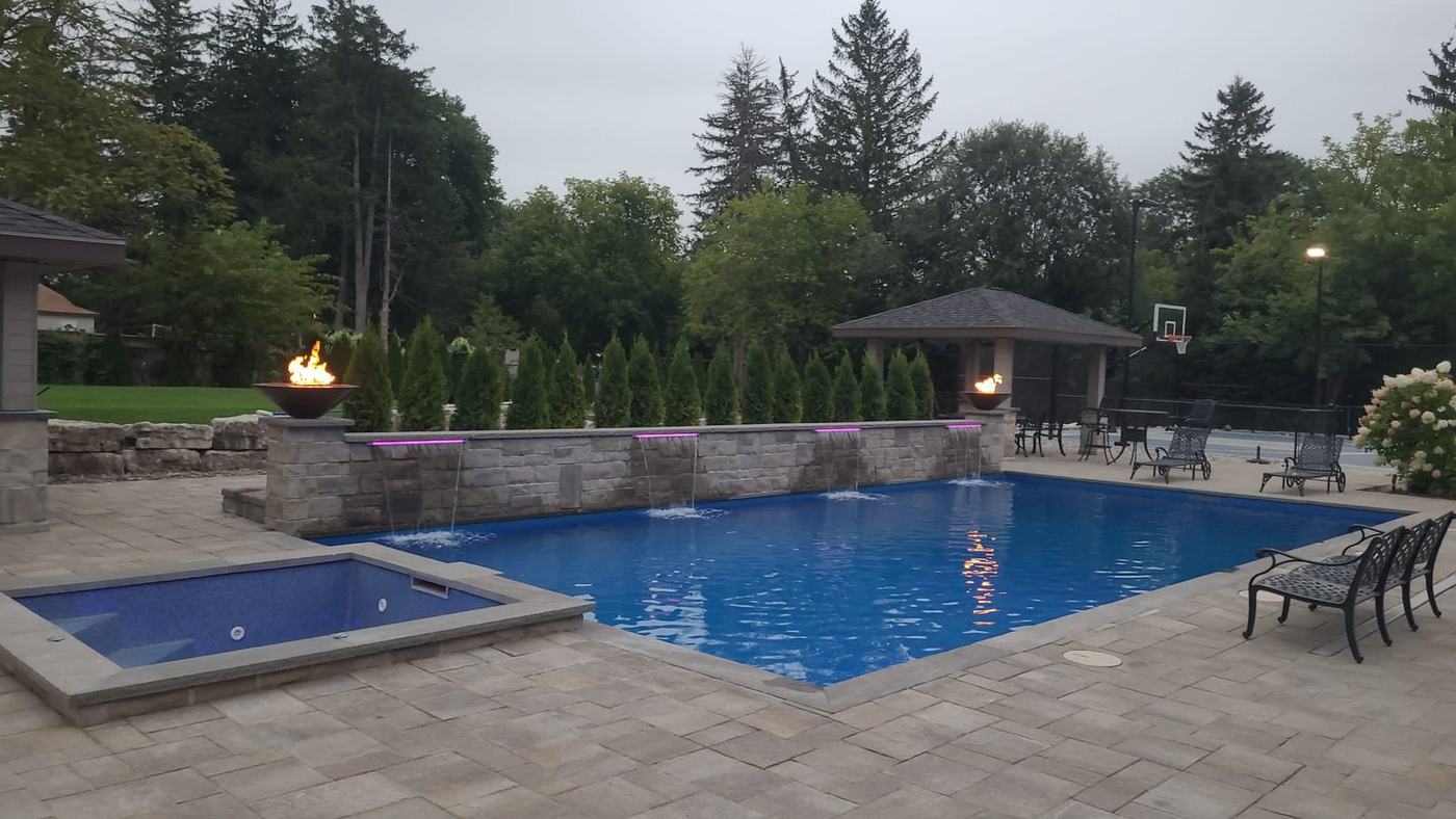 Paver pool deck with stone walls, fire bowls and a pavilion at dusk